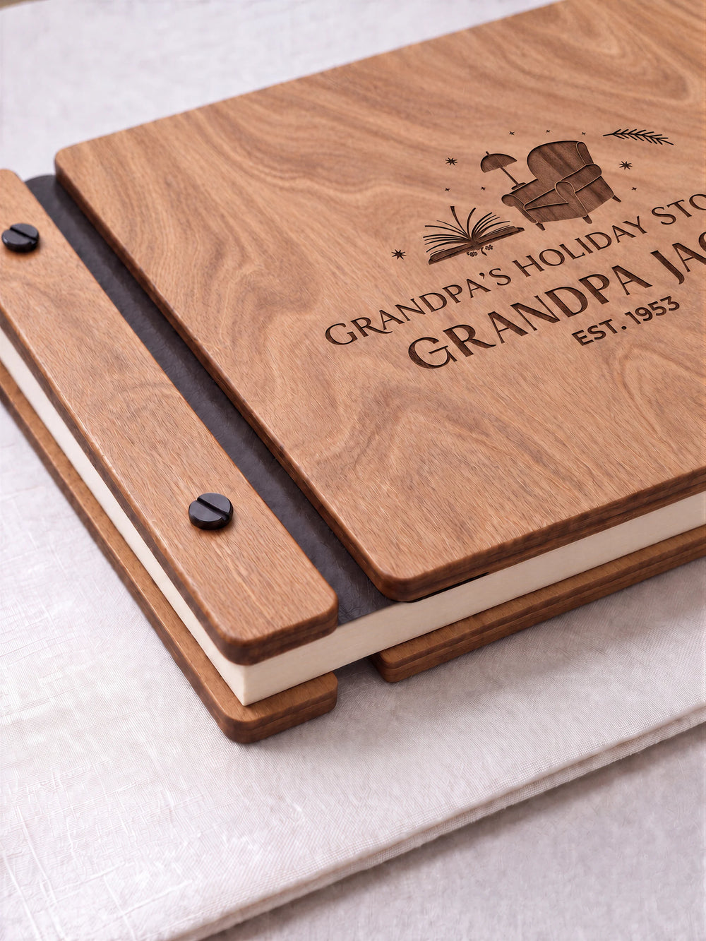 Close view of the hazelnut album’s engraved reading-chair design, espresso brown binding and black screws. Cream page edges and the separate lower wooden cover pieces are visible at the corner.