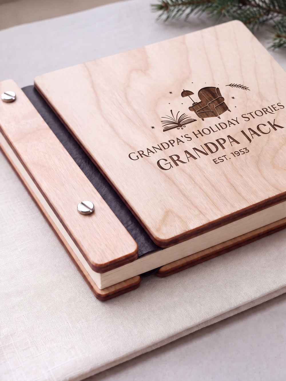 Close view of a Natural wood photo album with black binding and silver screws. Brown engraved artwork, layered cream pages and the gap between the lower wooden cover sections are visible.