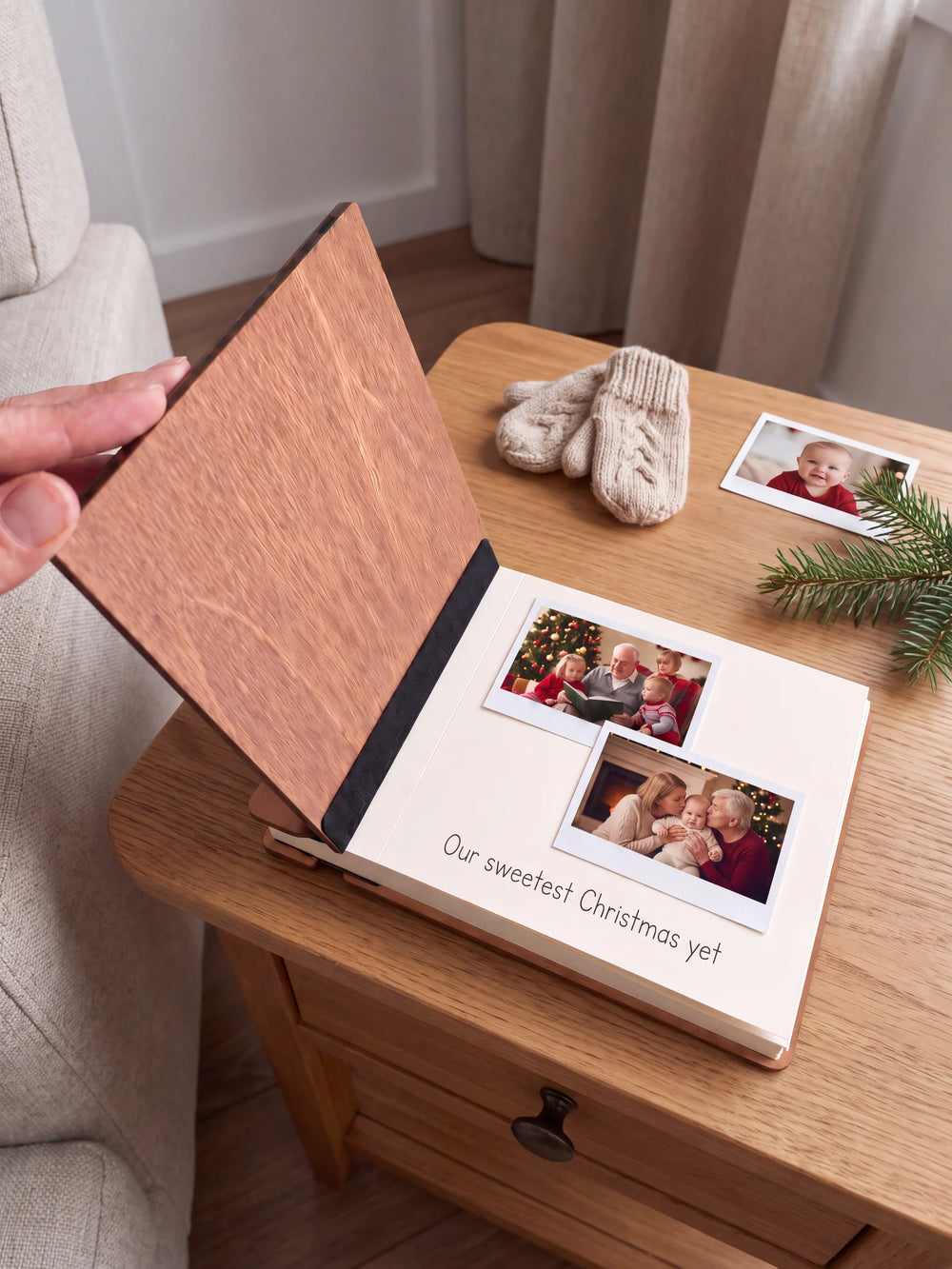 A hand lifts the Hazelnut album’s front cover, revealing a flat black inner fabric strip and a cream page arranged with instant photographs and a handwritten memory.