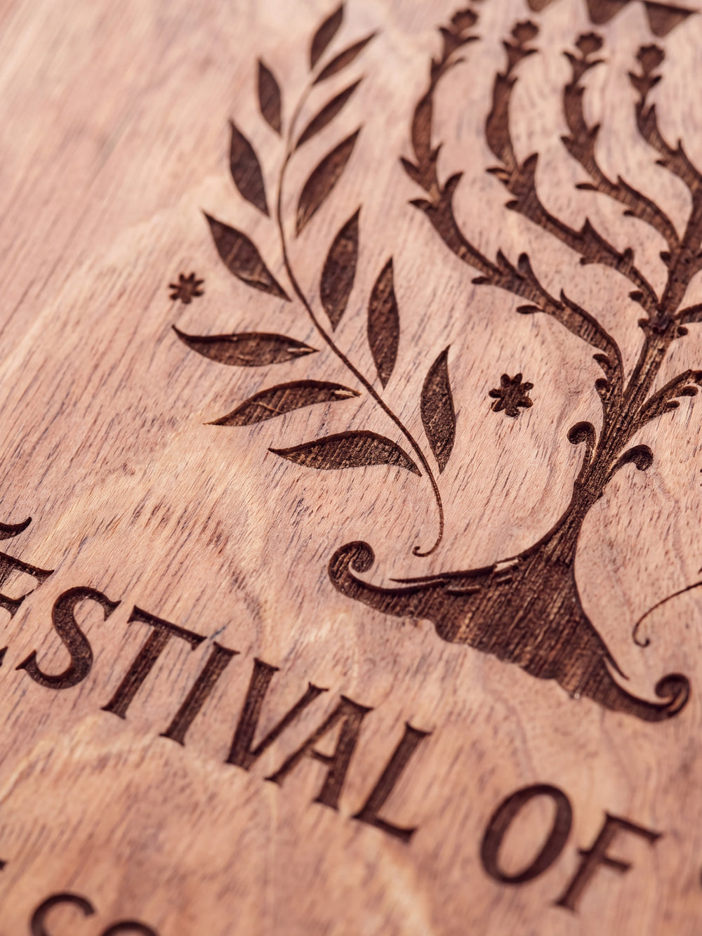 Close-up of the laser engraving on Hazelnut wood: a nine-branched menorah with leafy branches and the personalized text against the visible wood grain