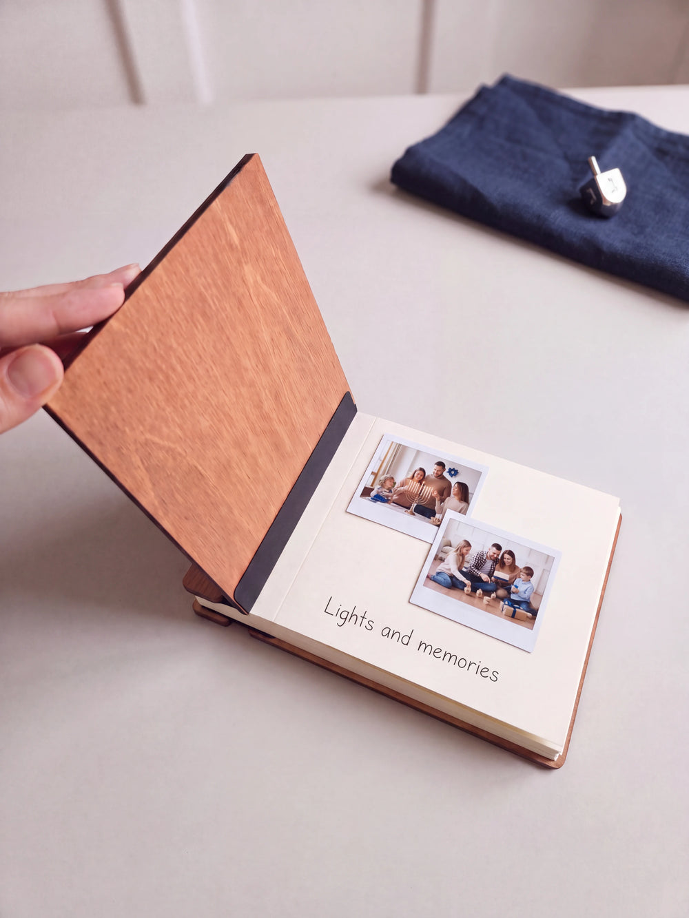 The Hazelnut Hanukkah photo memory book open on a table with instant photos and a short handwritten note on a cream page; the black hinge strip is visible