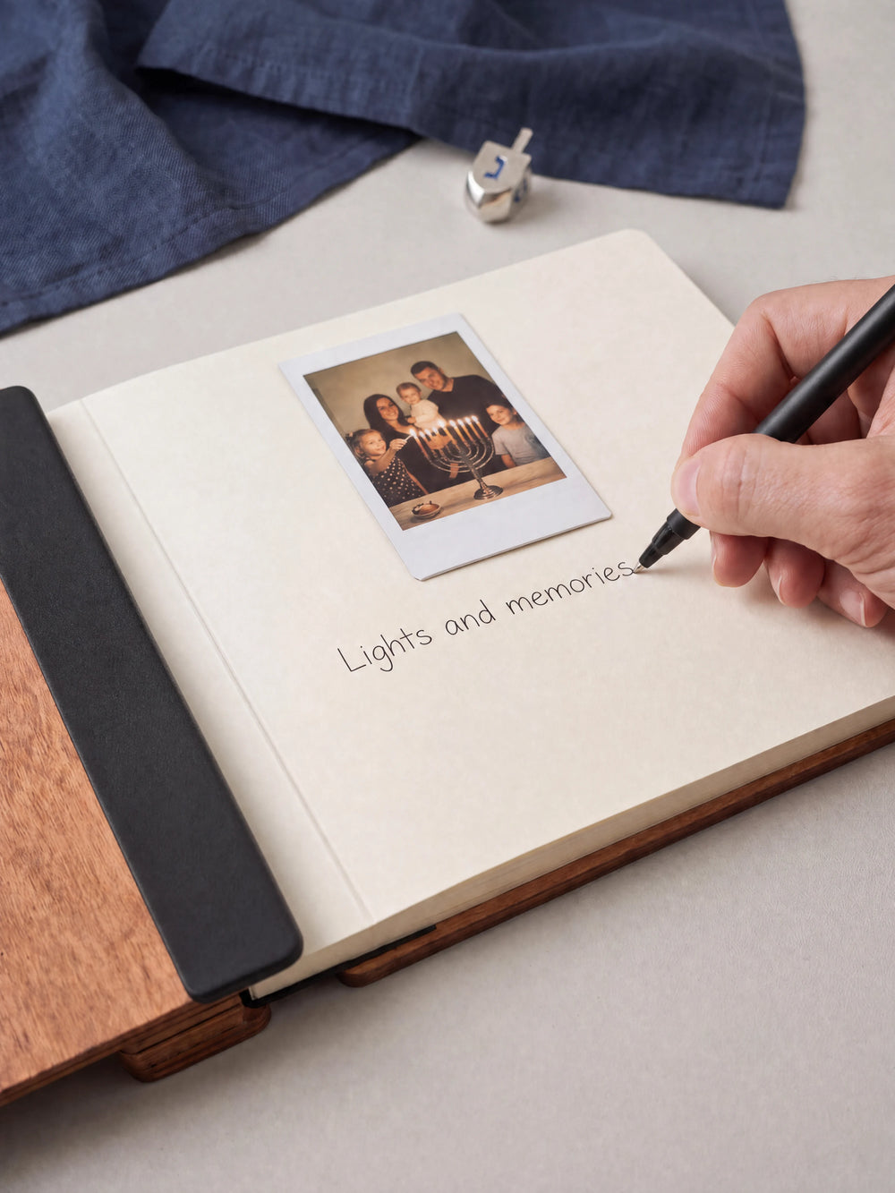 A hand writing a note in fine black pen beneath an instant photo on the cream page of the open Hazelnut Hanukkah photo memory book