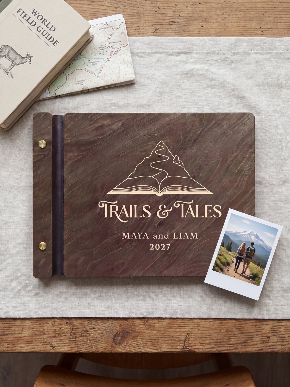 Dark brown Jacobean wooden album on a light surface, with cream engraving of a mountain rising from an open book and personalized cover wording. The full cover and left screw binding are visible.