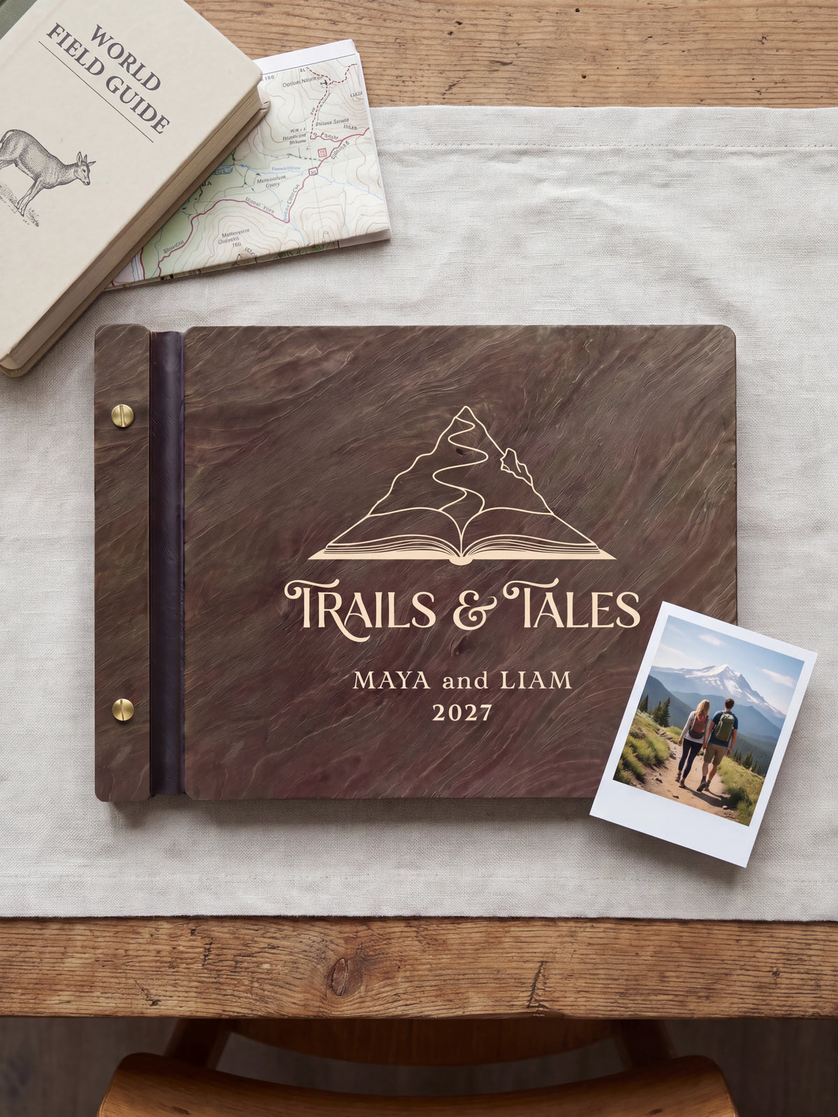 Dark brown Jacobean wooden album on a light surface, with cream engraving of a mountain rising from an open book and personalized cover wording. The full cover and left screw binding are visible.