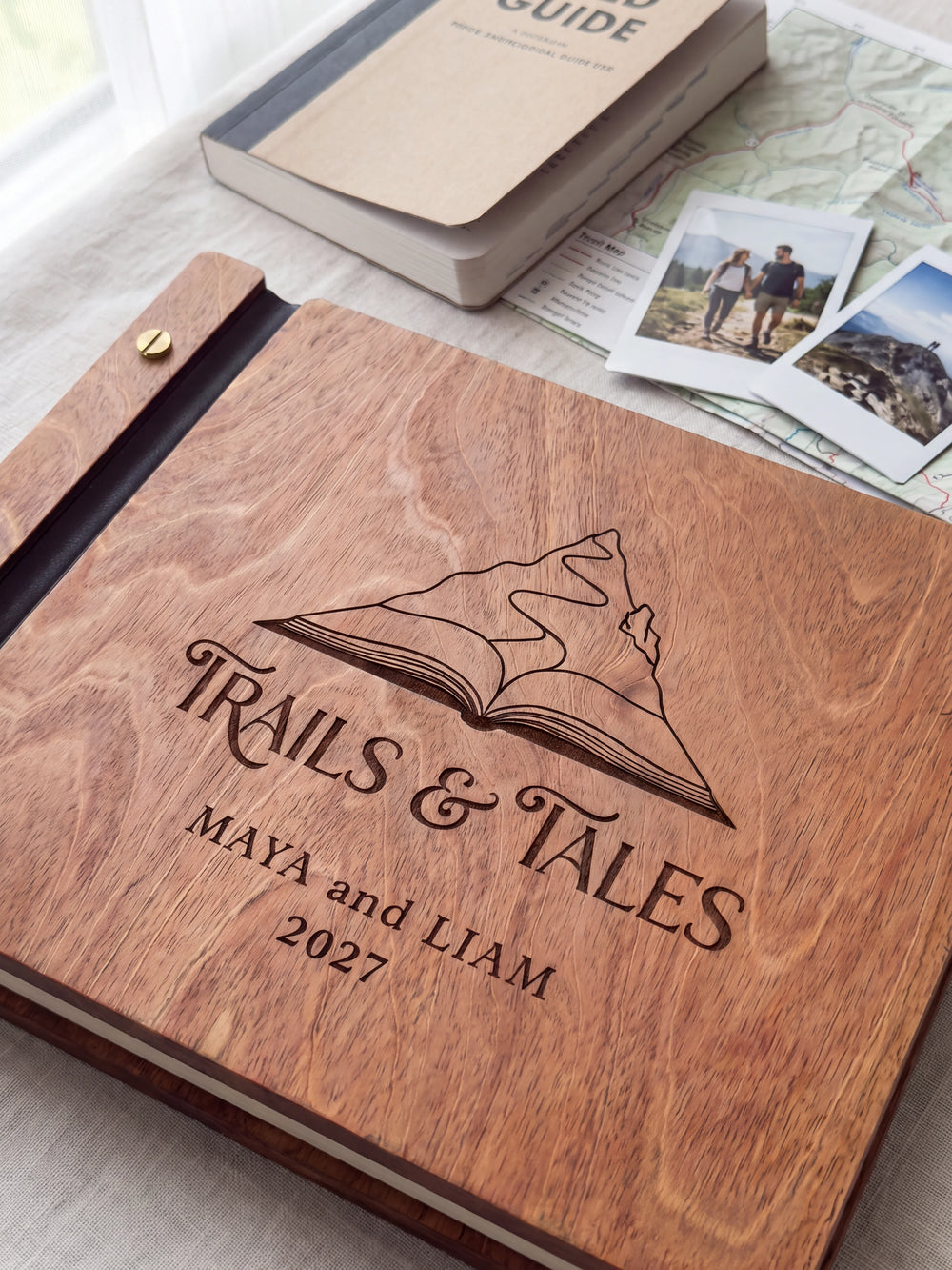 Close-up of a mountain rising from an open book engraved in dark brown on the Hazelnut wooden cover, showing the fine artwork and surrounding wood grain.