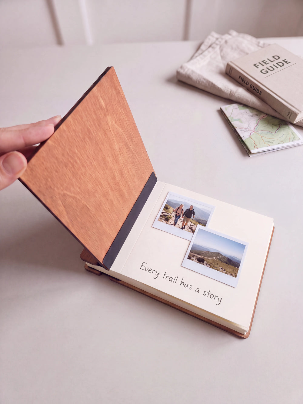 A hand lifts the Hazelnut album cover. Two hiking trip photos sit on a cream page above the handwritten note 