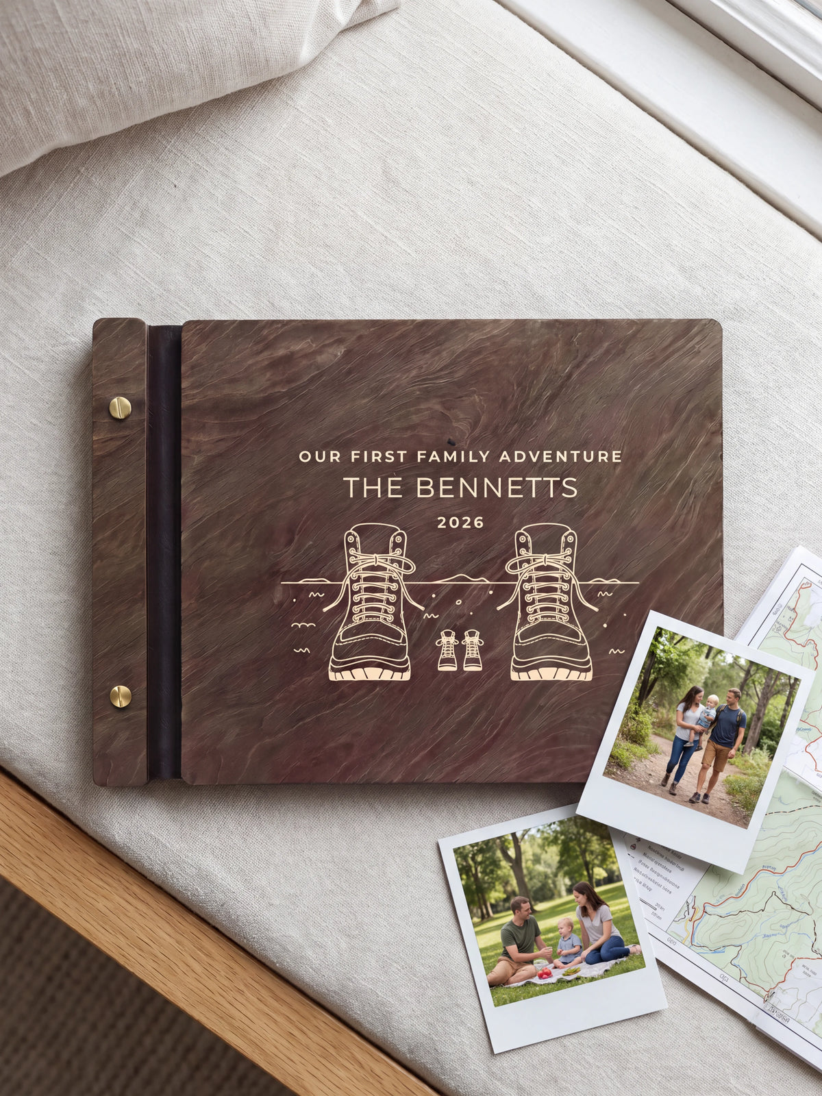 Dark brown Jacobean wooden album on a light surface, with cream engraving of adult and little hiking boots and personalized cover wording. The full cover and left screw binding are visible.