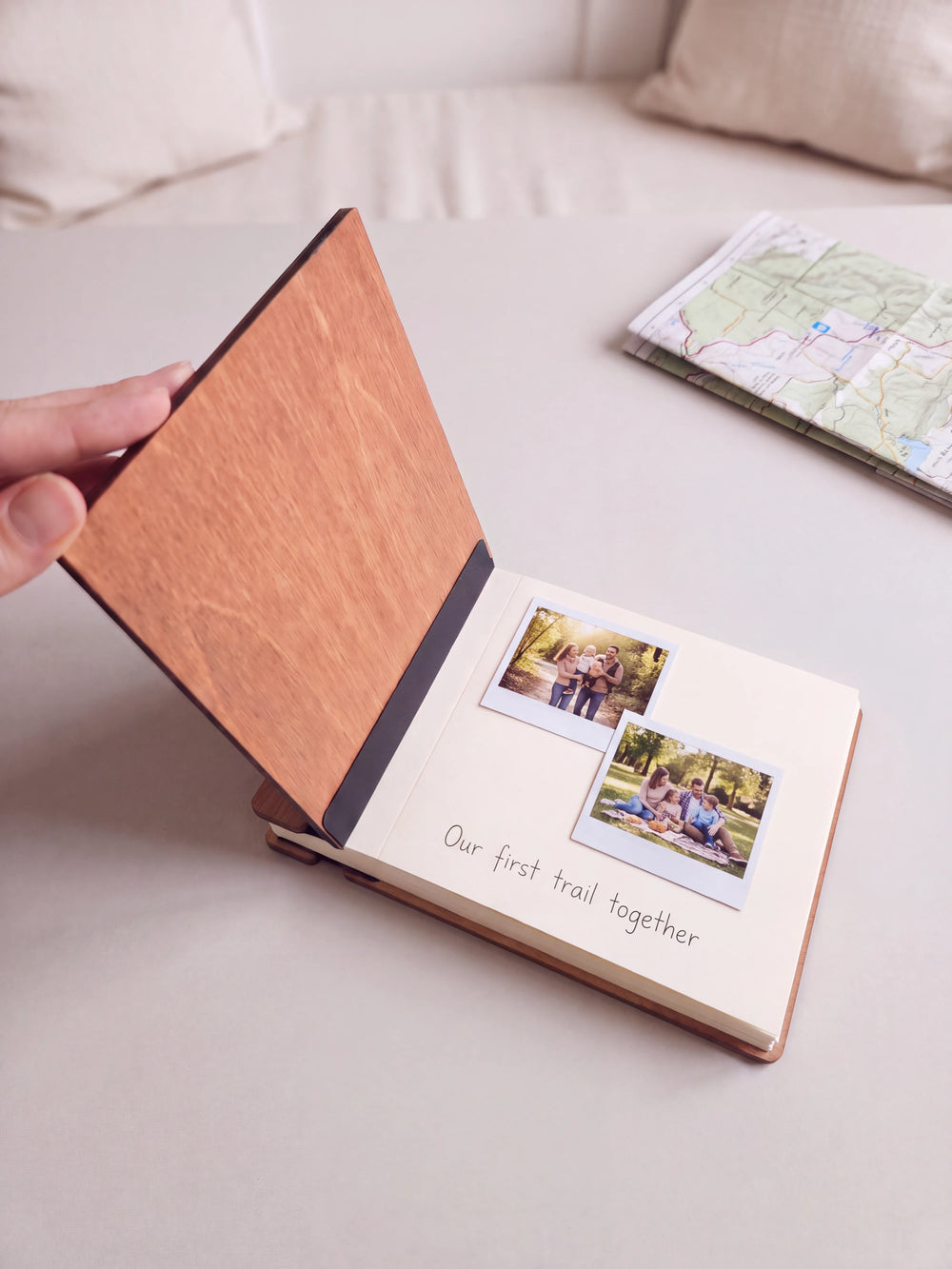 A hand lifts the Hazelnut album cover. Two family outdoor photos sit on a cream page above the handwritten note 