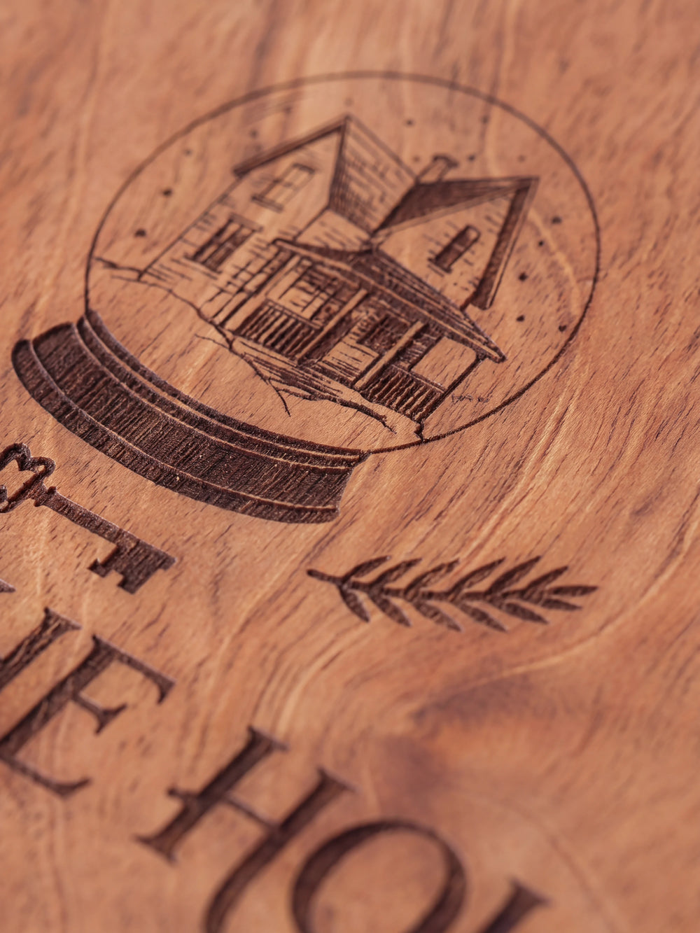 Close-up of the laser engraving on Hazelnut wood: a winter house inside a snow globe with evergreen sprigs and the personalized text against the visible wood grain