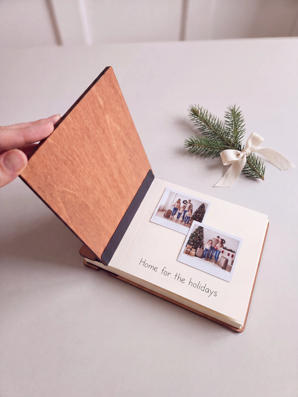 The Hazelnut Home for the Holidays photo book open on a table with instant photos and a short handwritten note on a cream page; the black hinge strip is visible