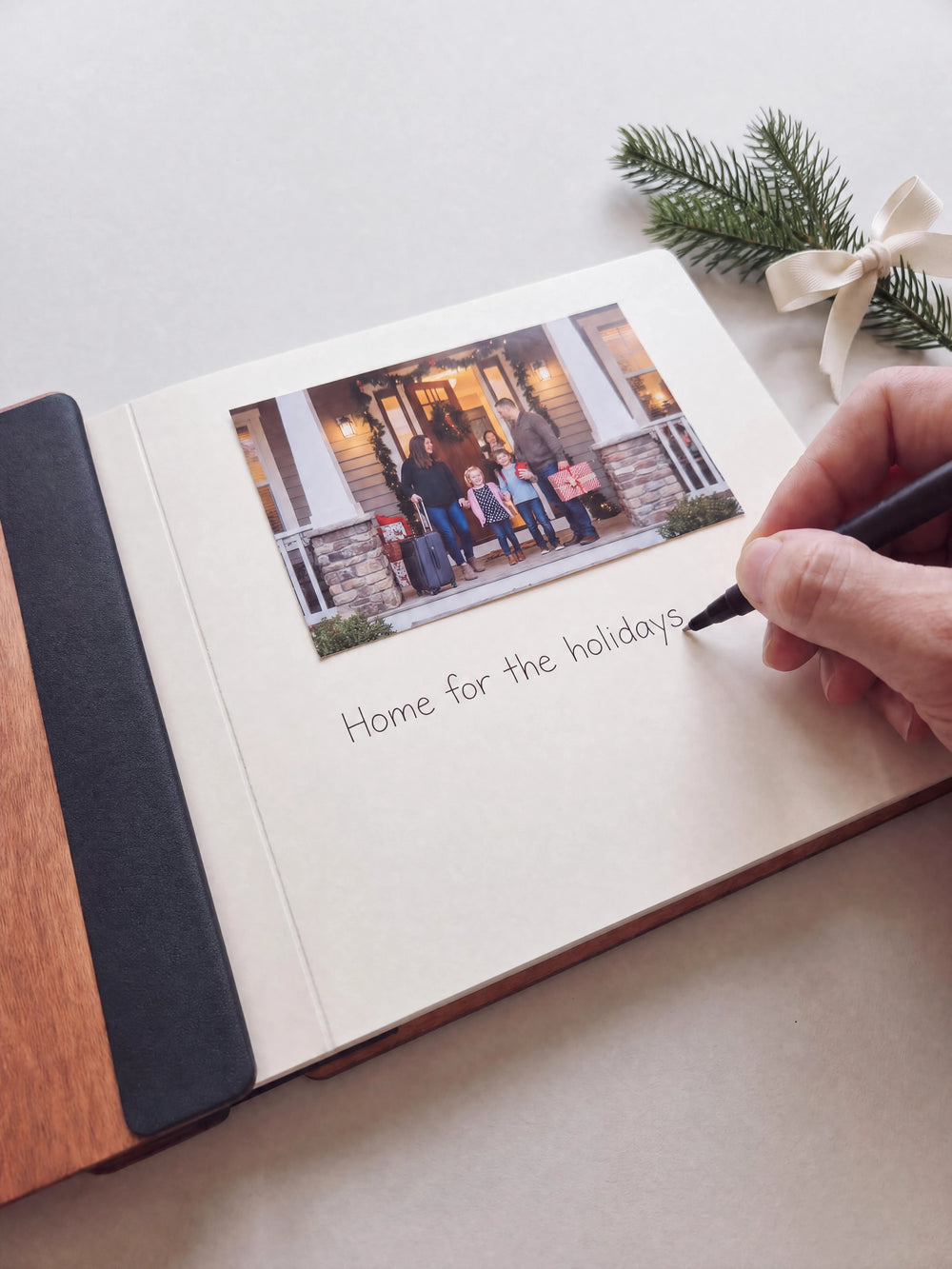 A hand writing a note in fine black pen beneath an instant photo on the cream page of the open Hazelnut Home for the Holidays photo book