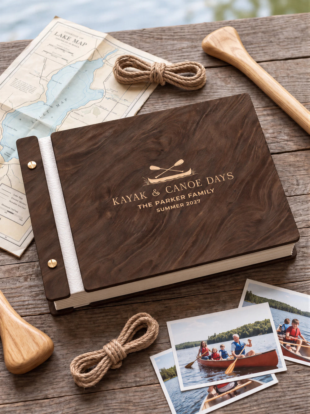 Jacobean wooden album with cream laser engraving of canoe and crossed paddles. The full personalized cover rests on a styled surface, with ivory binding and gold screws.