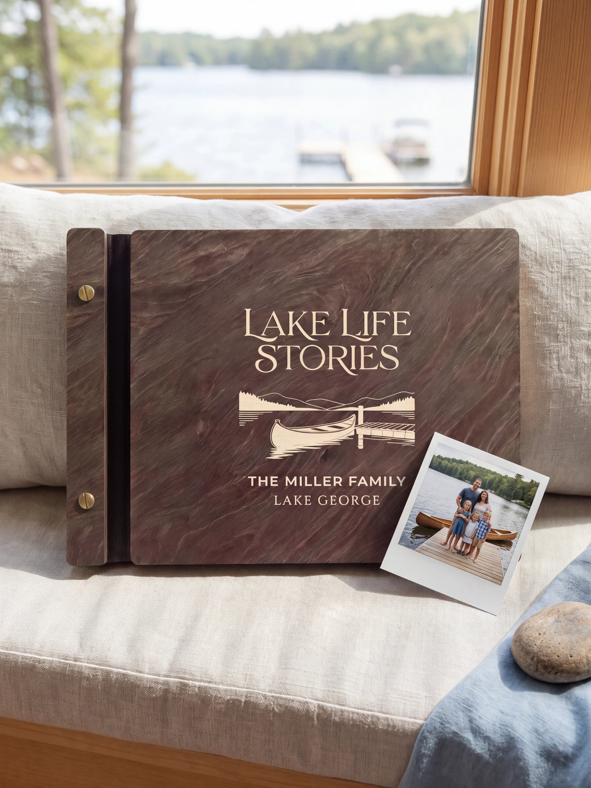 Dark brown Jacobean wooden album on a light surface, with cream engraving of a canoe beside a lakeside dock and personalized cover wording. The full cover and left screw binding are visible.