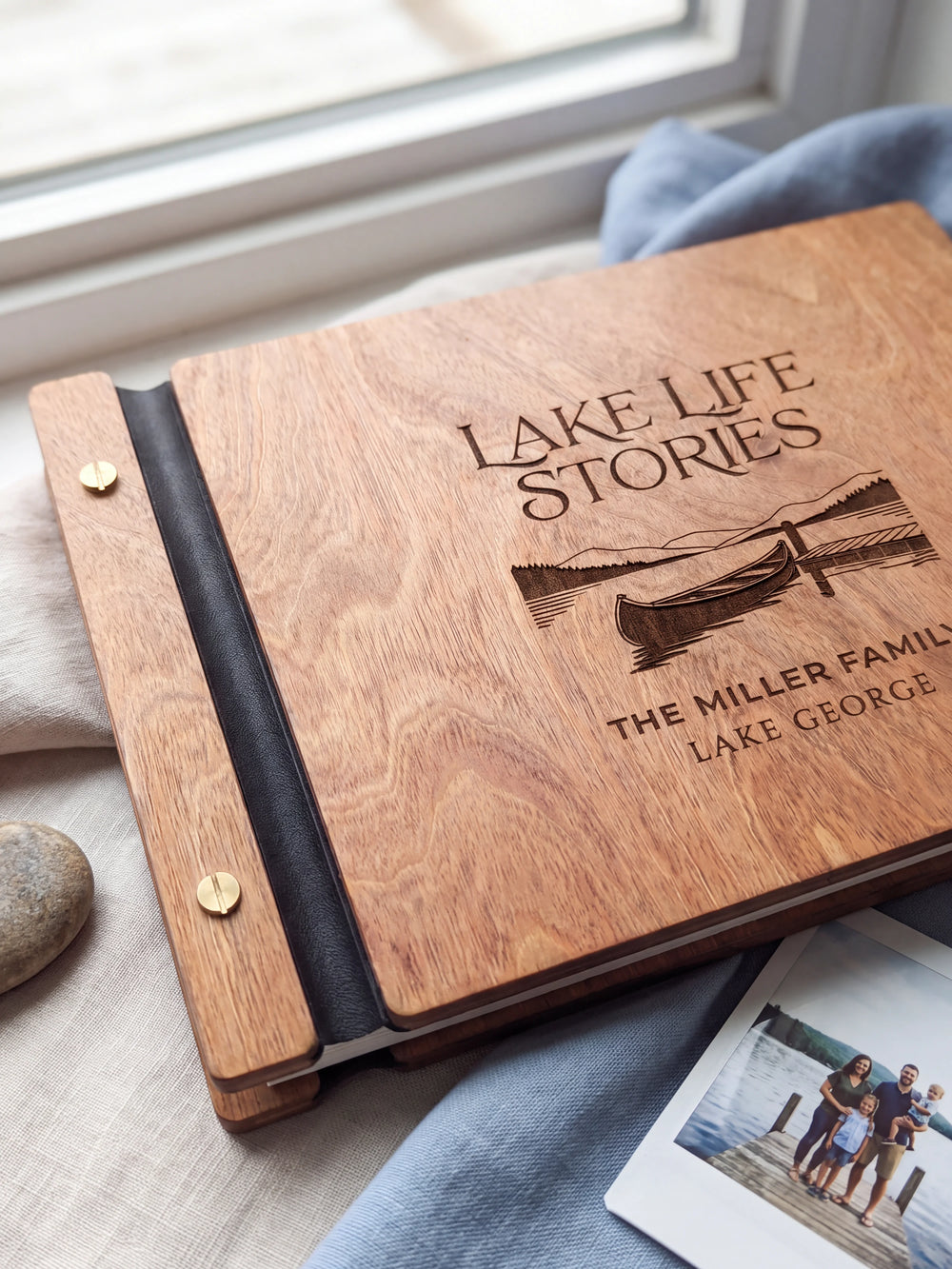 Close-up of a canoe beside a lakeside dock engraved in dark brown on the Hazelnut wooden cover, showing the fine artwork and surrounding wood grain.