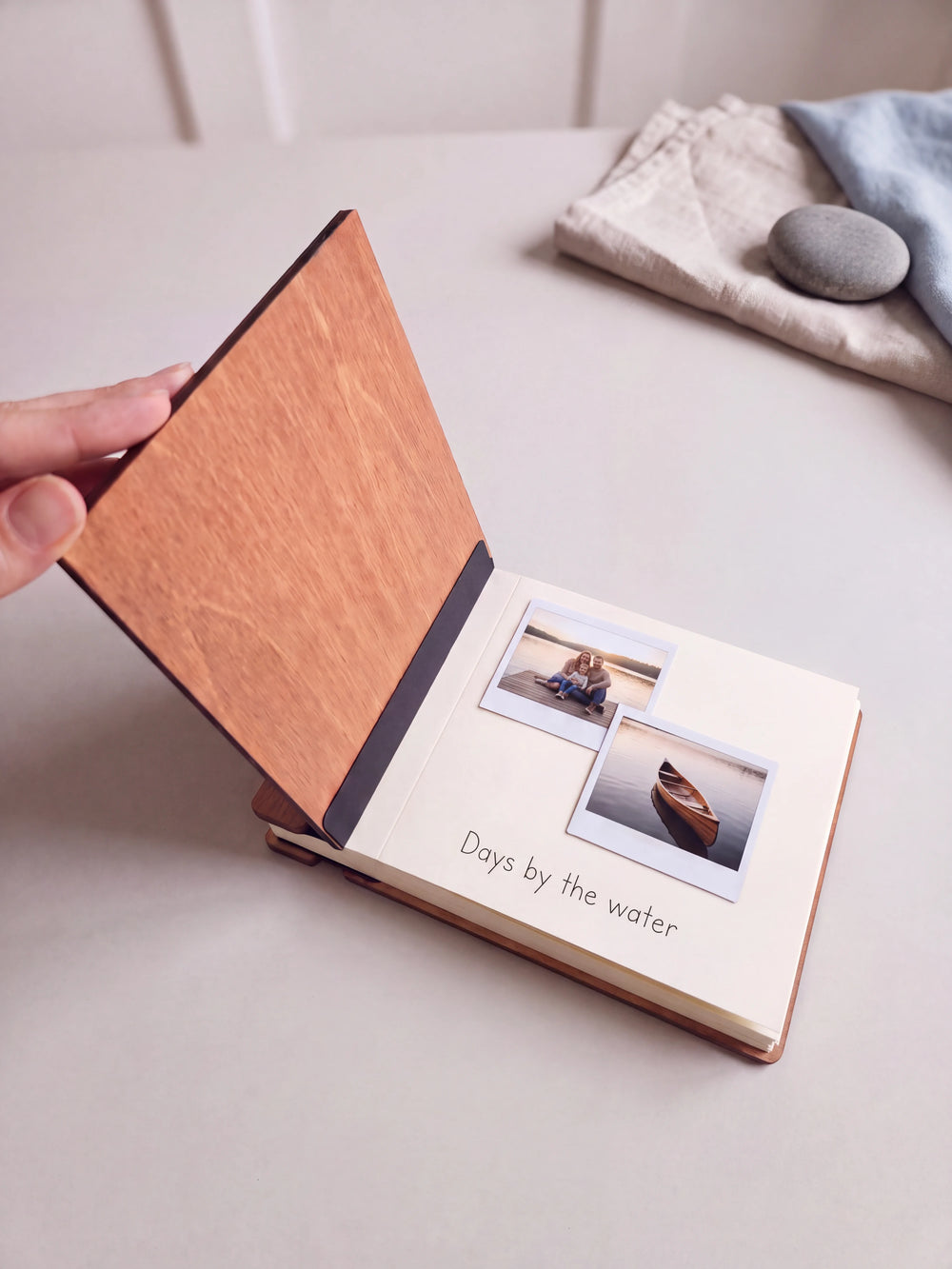 A hand lifts the Hazelnut album cover. Two family lake vacation photos sit on a cream page above the handwritten note 