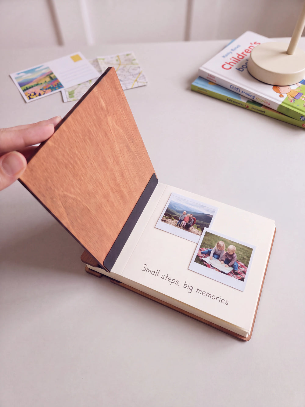 A hand lifts the Hazelnut album cover. Two family travel photos sit on a cream page above the handwritten note 