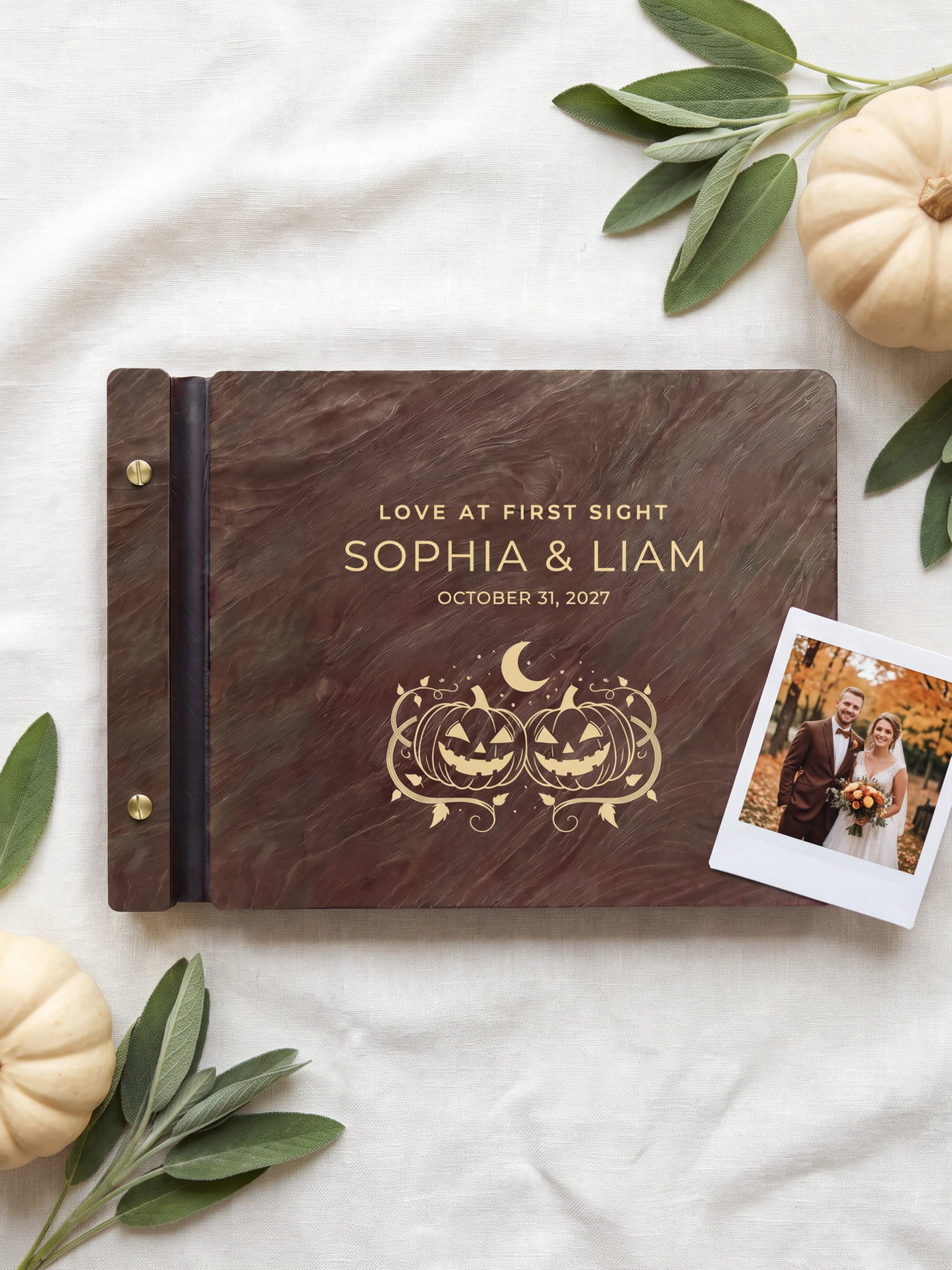 Jacobean wood Love at First Sight photo guest book lying flat on ivory linen, the cover engraved with “LOVE AT FIRST SIGHT”, “SOPHIA & LIAM” and “OCTOBER 31, 2027”; two gold-tone screws along the black vegan leather spine