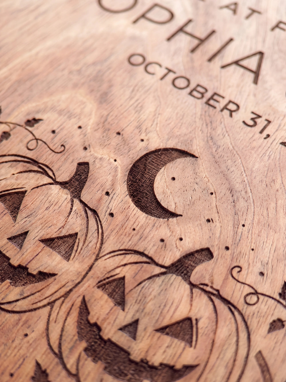 Close-up of the laser engraving on Hazelnut wood: two smiling carved pumpkins under a crescent moon and the personalized text against the visible wood grain
