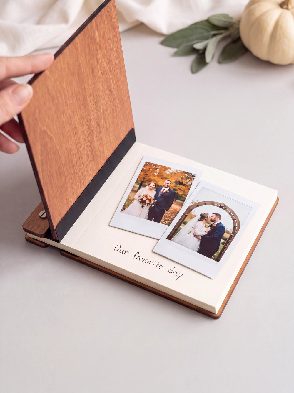 The Hazelnut Love at First Sight photo guest book open on a table with instant photos and a short handwritten note on a cream page; the black hinge strip is visible