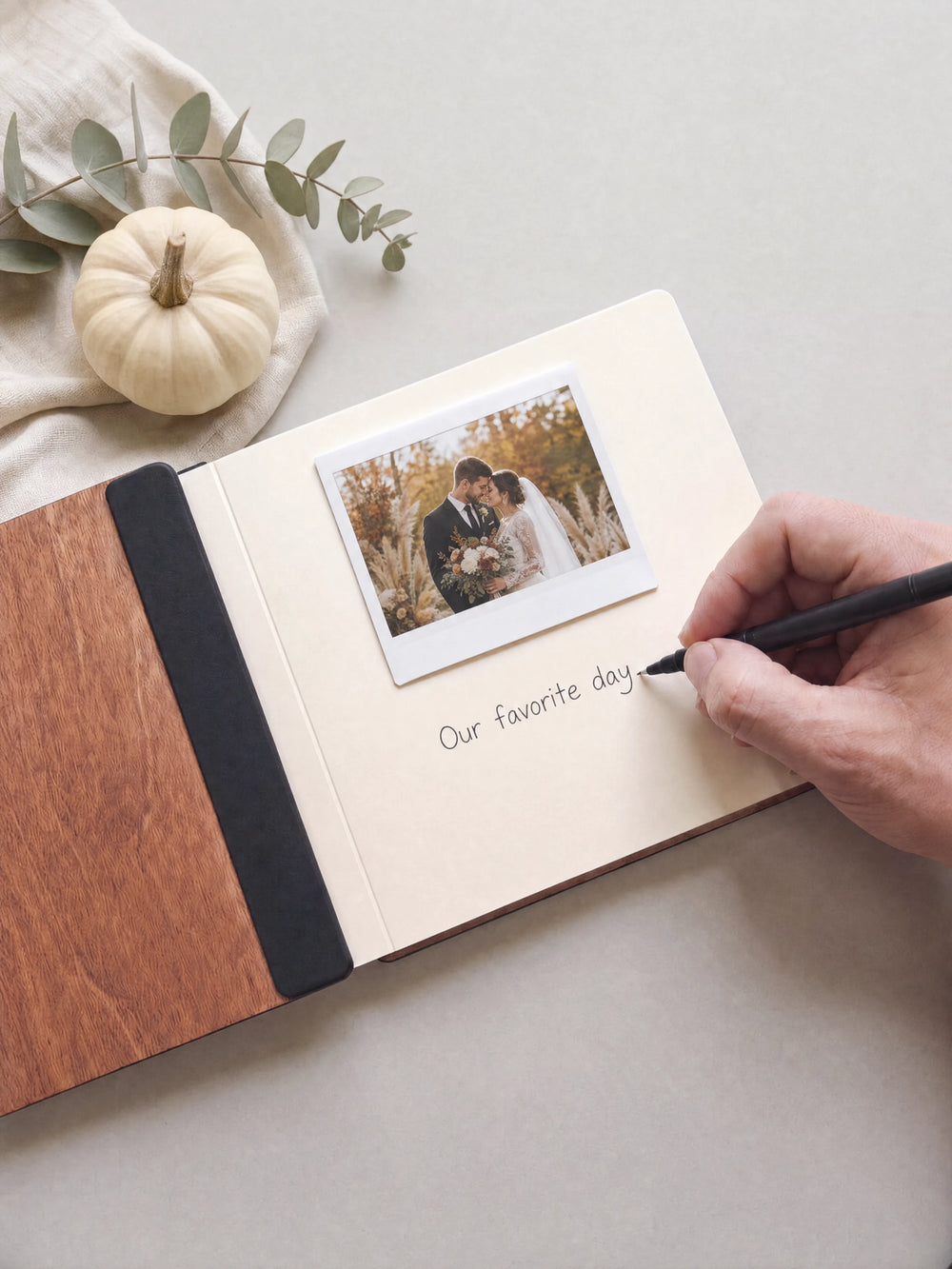 A hand writing a note in fine black pen beneath an instant photo on the cream page of the open Hazelnut Love at First Sight photo guest book
