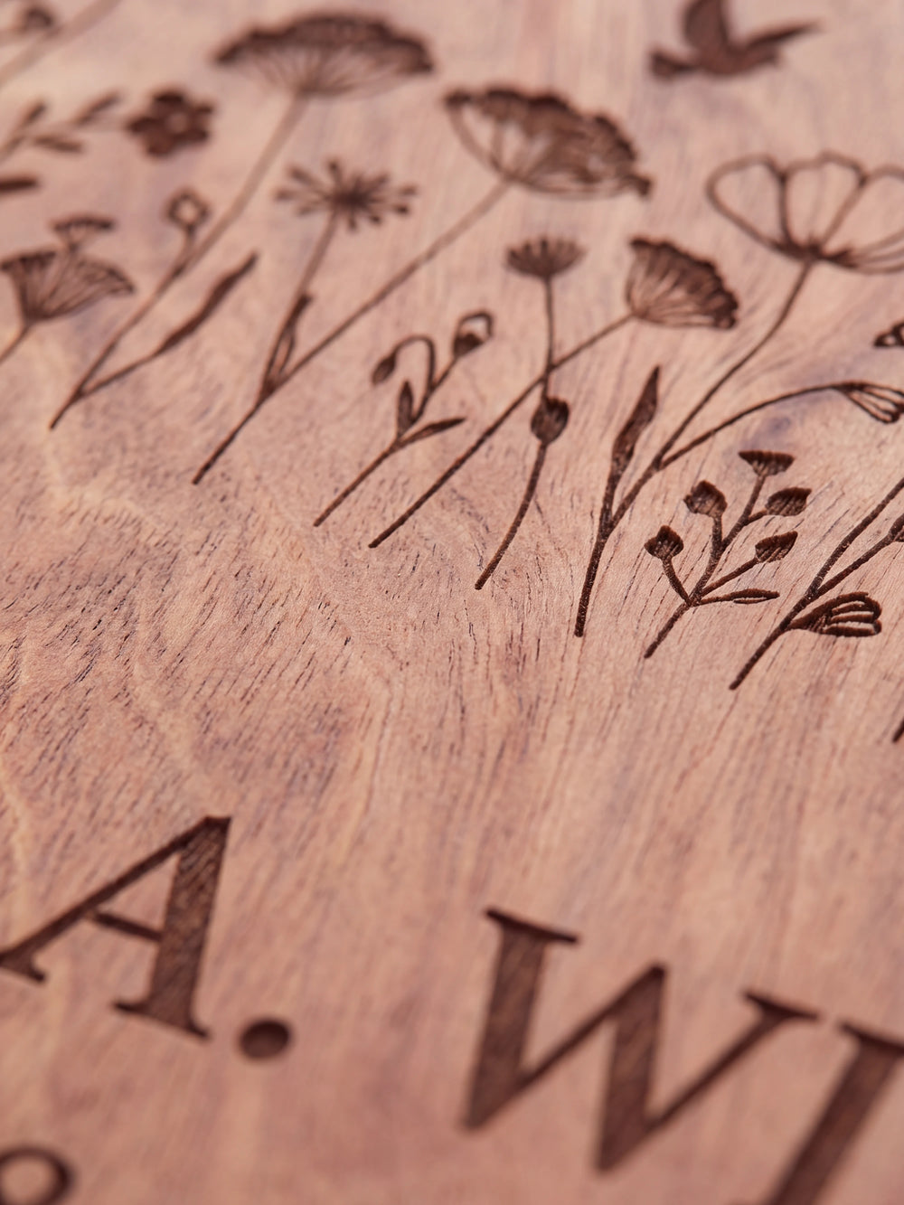 Close-up of the laser engraving on Hazelnut wood: a wildflower meadow with a small dove and the personalized text against the visible wood grain