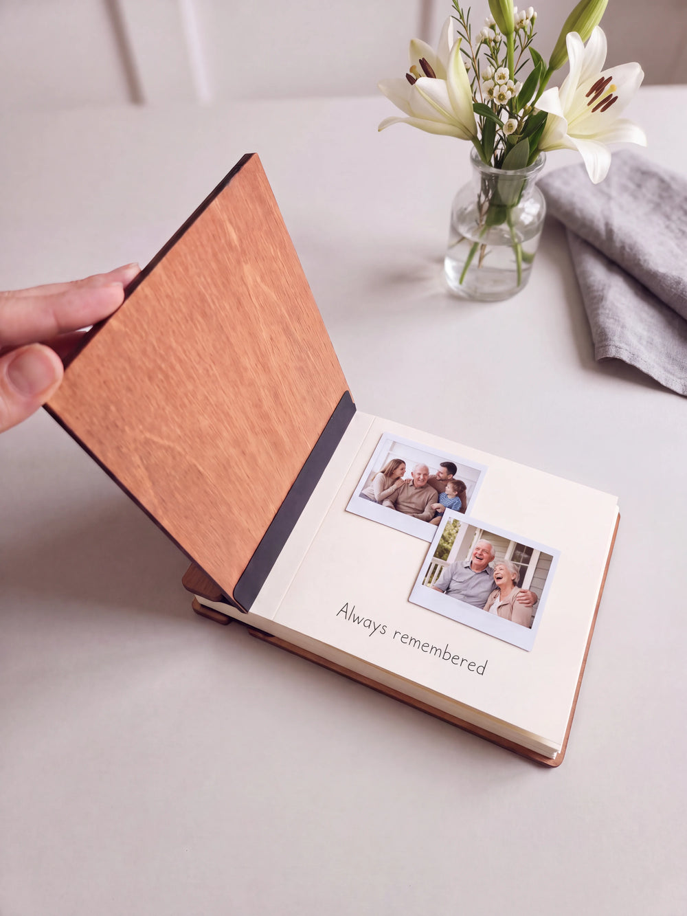 The Hazelnut memorial photo guest book open on a table with instant photos and a short handwritten note on a cream page; the black hinge strip is visible