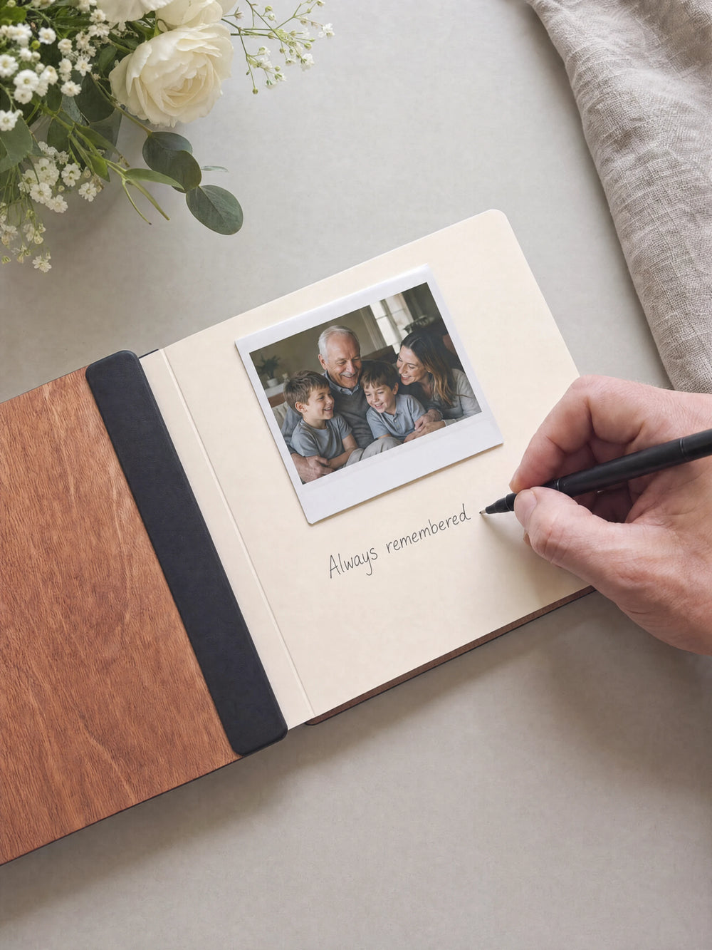 A hand writing a note in fine black pen beneath an instant photo on the cream page of the open Hazelnut memorial photo guest book