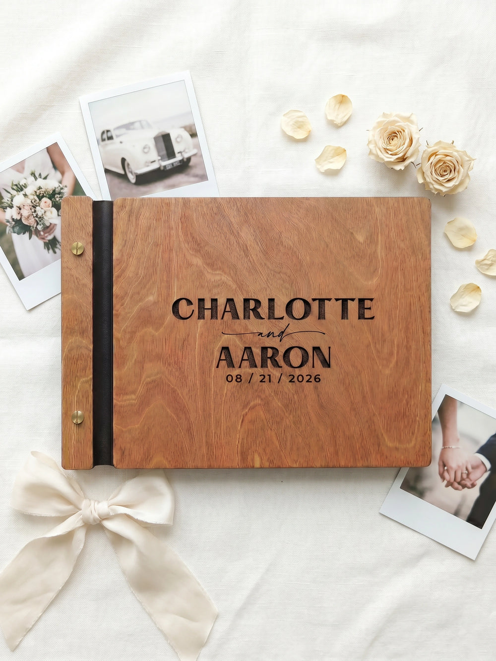 Hazelnut wood wedding photo guest book engraved Charlotte and Aaron 08 / 21 / 2026 in bold letters, on a white cloth with instant photos, roses and a ribbon