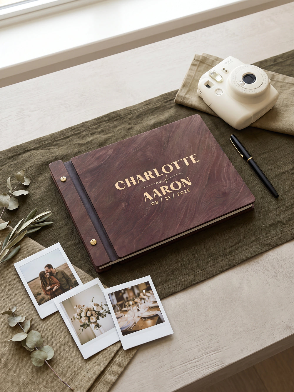 Natural wood Charlotte and Aaron photo guest book on a table with an instant camera, a pen and two instant photos