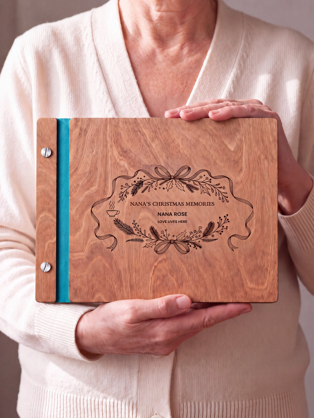 Two hands hold a Hazelnut wooden photo album. The NANA’S CHRISTMAS MEMORIES cover design has brown engraving, turquoise binding and silver screws.
