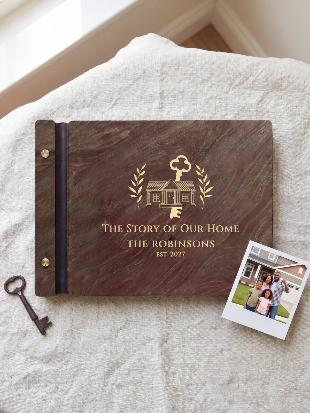 Jacobean wood The Story of Our Home photo book lying flat on natural linen, the cover engraved with “THE STORY OF OUR HOME”, “THE ROBINSONS” and “EST. 2027”; two gold-tone screws along the black vegan leather spine