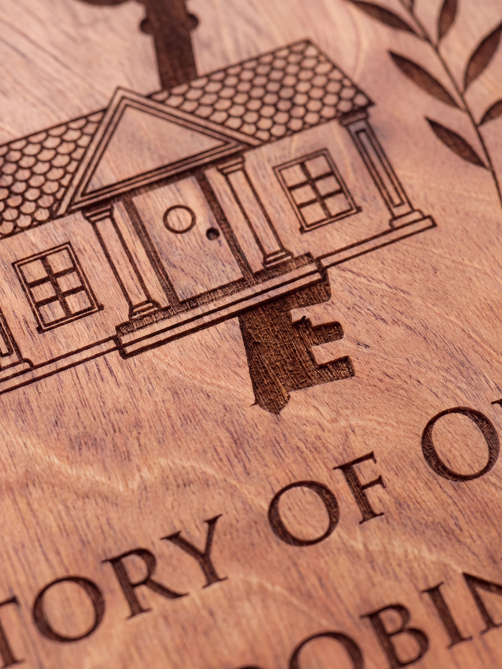 Close-up of the laser engraving on Hazelnut wood: a house with a large old-fashioned key and leafy branches and the personalized text against the visible wood grain