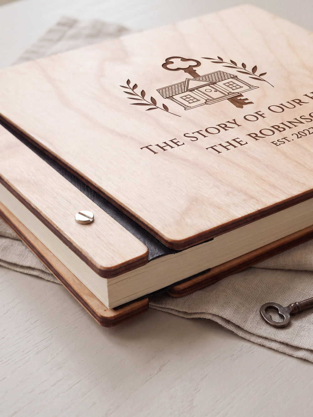 Close-up of a polished silver screw in the Natural wood strip beside the black vegan leather binding, the cream sheet stack visible below