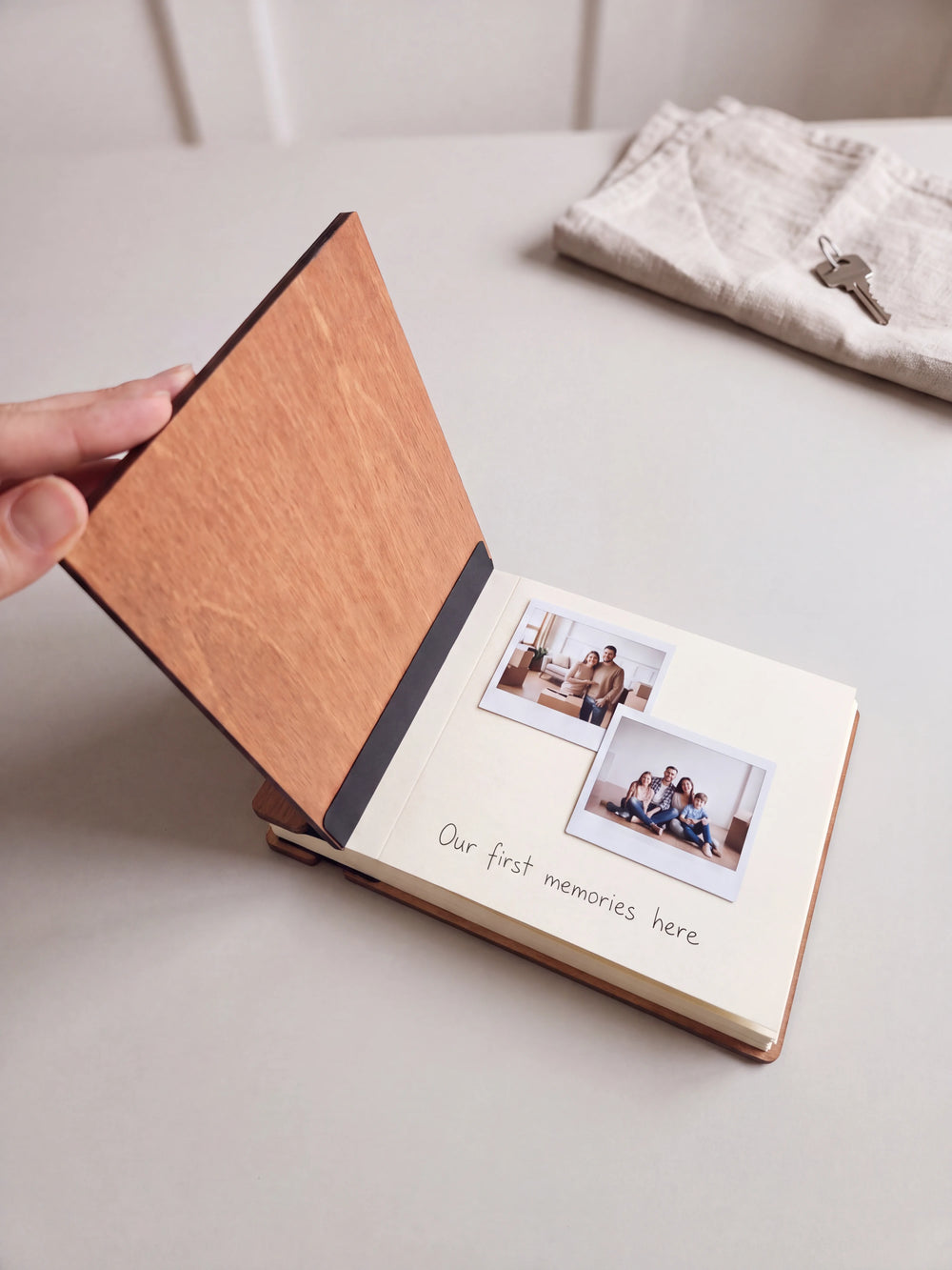 The Hazelnut The Story of Our Home photo book open on a table with instant photos and a short handwritten note on a cream page; the black hinge strip is visible