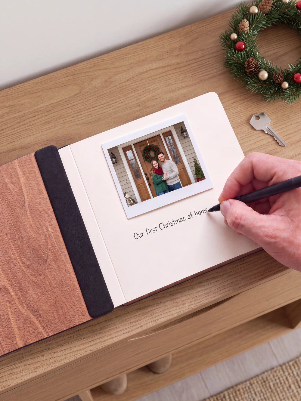 An open Hazelnut album with a photograph on a cream page. A hand writes a memory beneath it; a flat black fabric strip runs along the inner wooden cover.