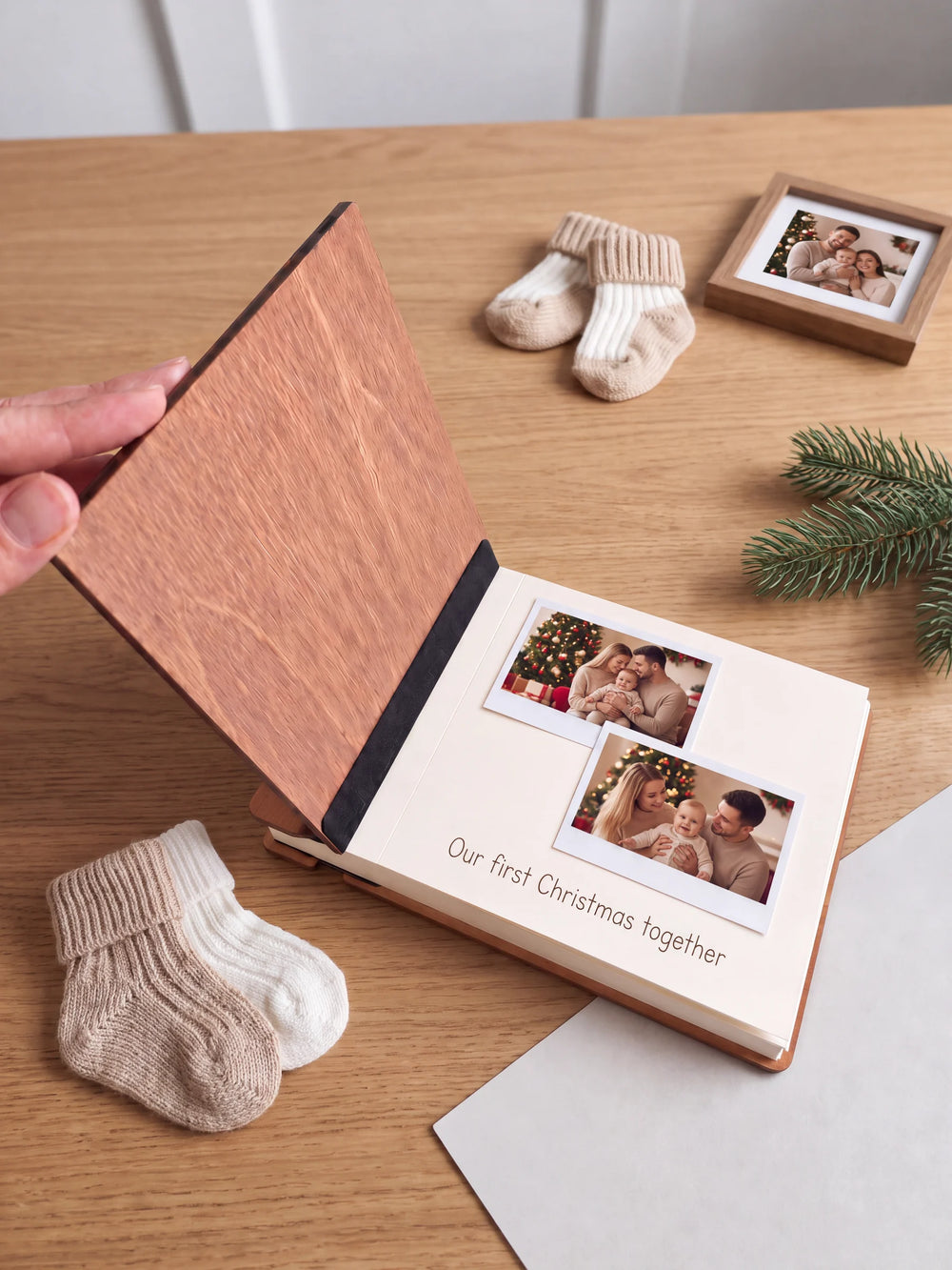 A hand lifts the Hazelnut album’s front cover, revealing a flat black inner fabric strip and a cream page arranged with instant photographs and a handwritten memory.