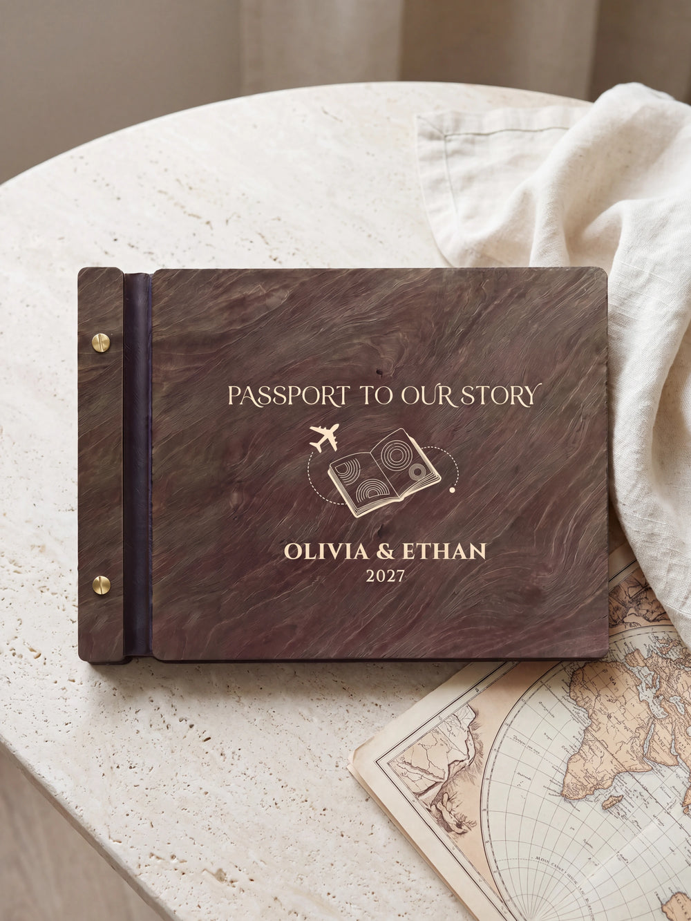 Dark brown Jacobean wooden album on a light surface, with cream engraving of a passport and airplane and personalized cover wording. The full cover and left screw binding are visible.