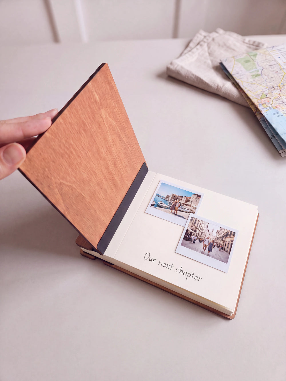 A hand lifts the Hazelnut album cover. Two couple vacation photos sit on a cream page above the handwritten note 
