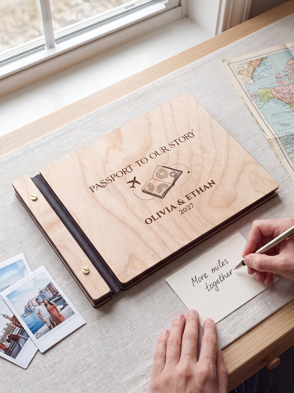A Natural wooden album showing a passport and airplane rests beside a separate gift card. A hand writes 