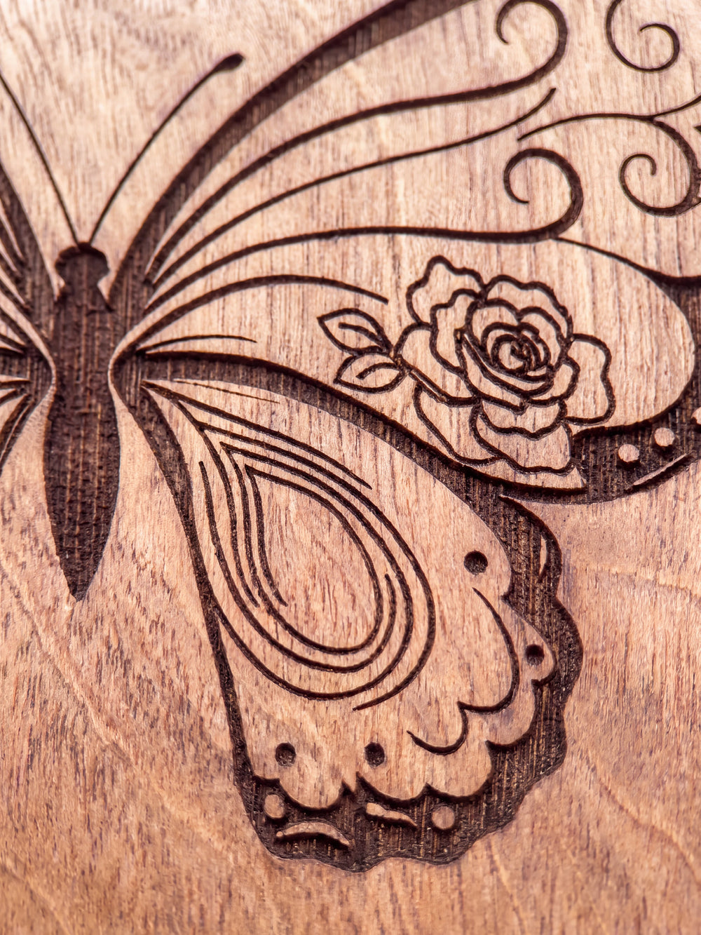 Close-up of the laser engraving on Hazelnut wood: an ornate butterfly topped with a small crown and the personalized text against the visible wood grain