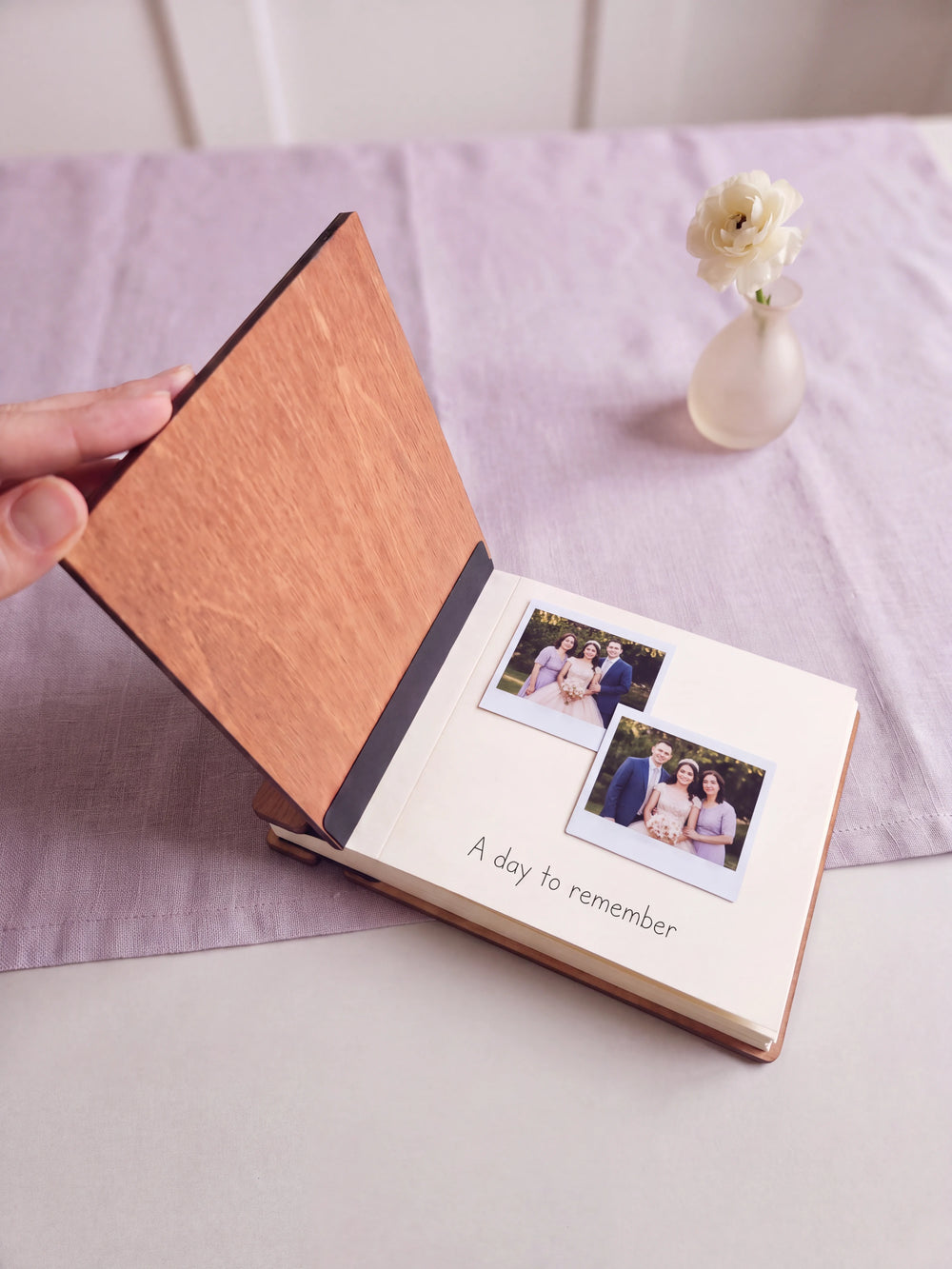 The Hazelnut quinceañera photo guest book open on a table with instant photos and a short handwritten note on a cream page; the black hinge strip is visible