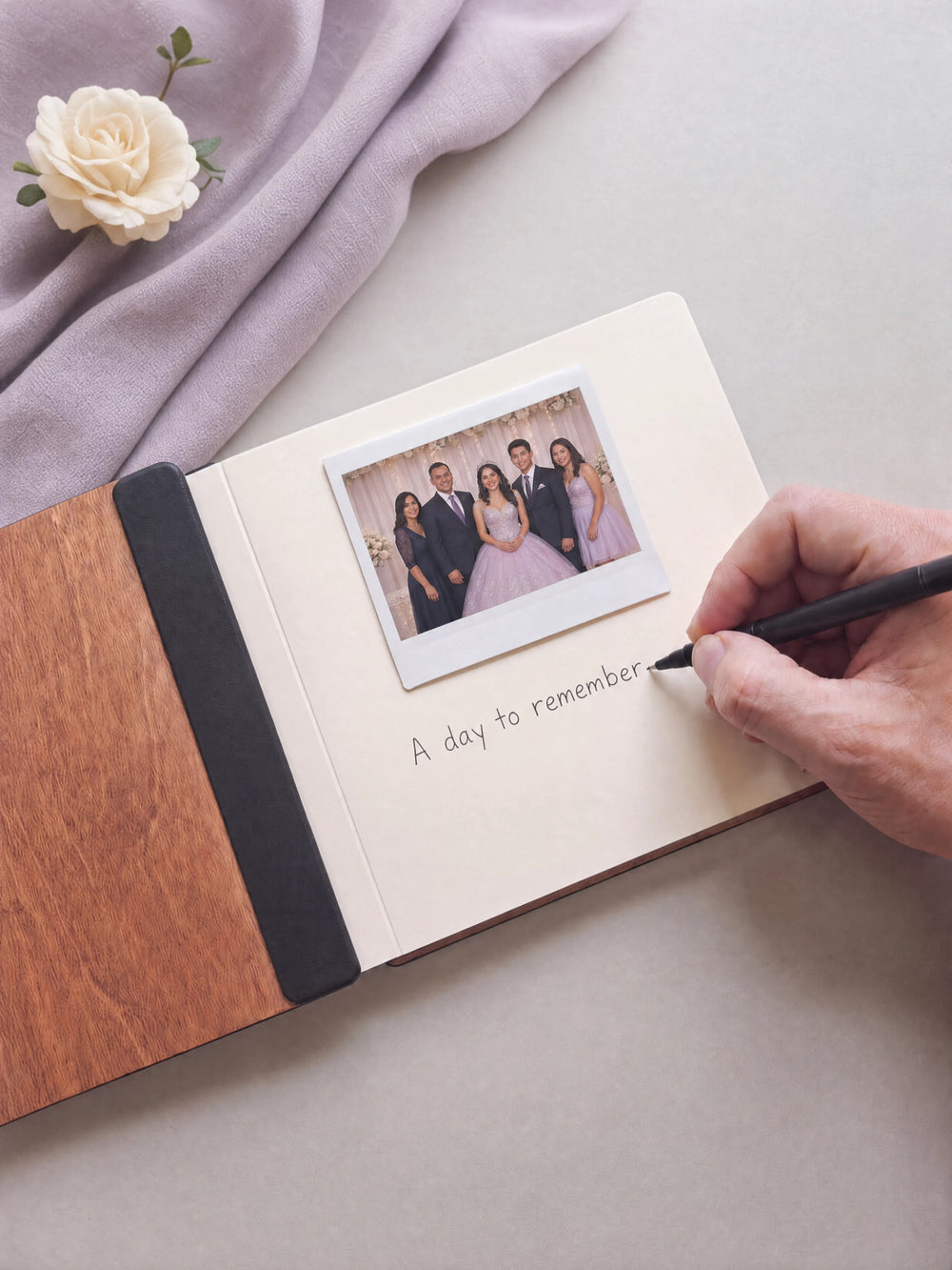 A hand writing a note in fine black pen beneath an instant photo on the cream page of the open Hazelnut quinceañera photo guest book
