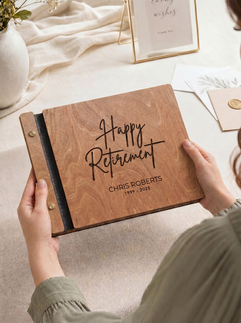 Hazelnut wood Happy Retirement photo guest book engraved Chris Roberts 1999 - 2025, held in two hands over a table with a card frame