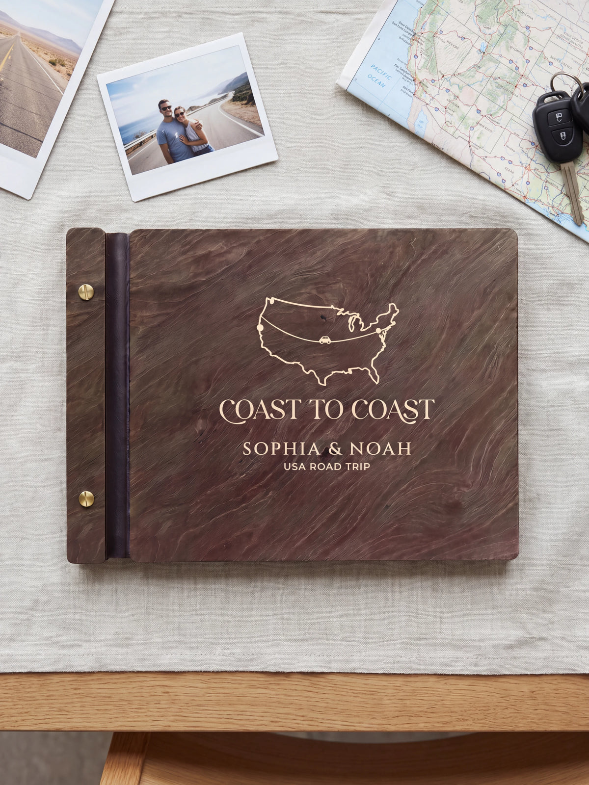 Dark brown Jacobean wooden album on a light surface, with cream engraving of a USA outline map and road-trip route and personalized cover wording. The full cover and left screw binding are visible.