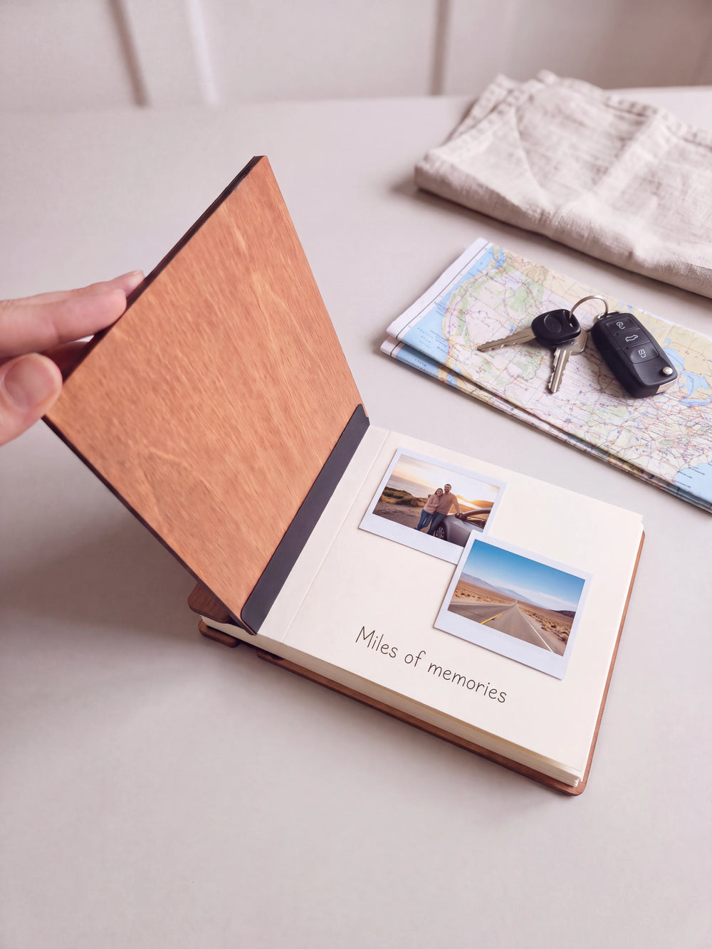 A hand lifts the Hazelnut album cover. Two road trip photos sit on a cream page above the handwritten note 