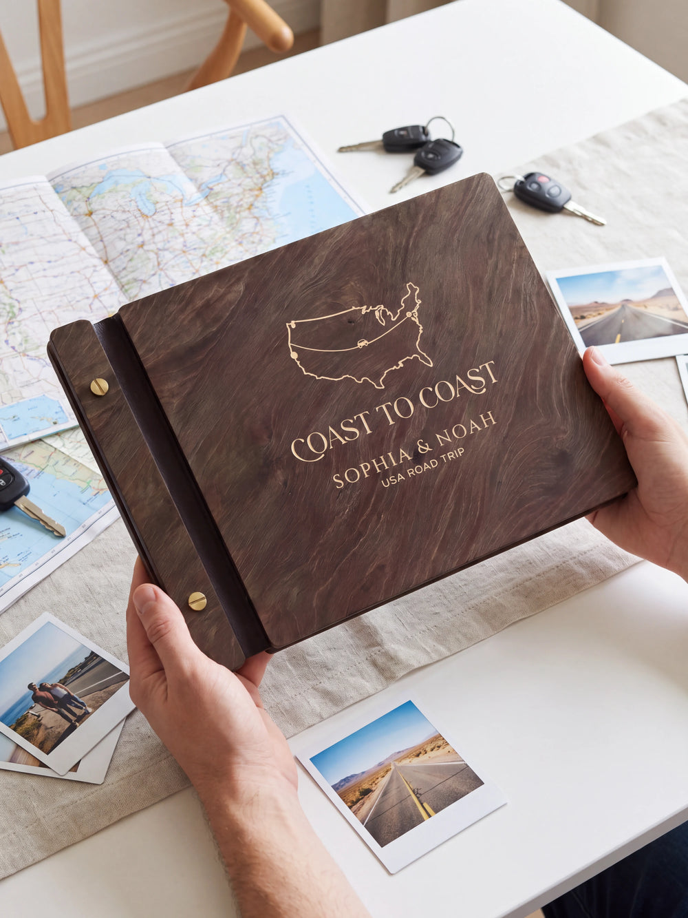 Two hands present a dark brown Jacobean wooden album, with the full cream-engraved USA outline map and road-trip route design and personalized cover wording facing the camera.