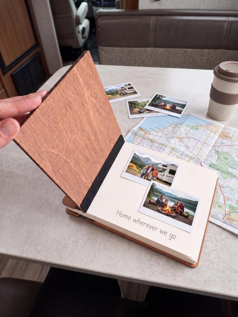A hand lifts the Hazelnut album’s front cover, revealing a flat black inner fabric strip and a cream page arranged with instant photographs and a handwritten memory.