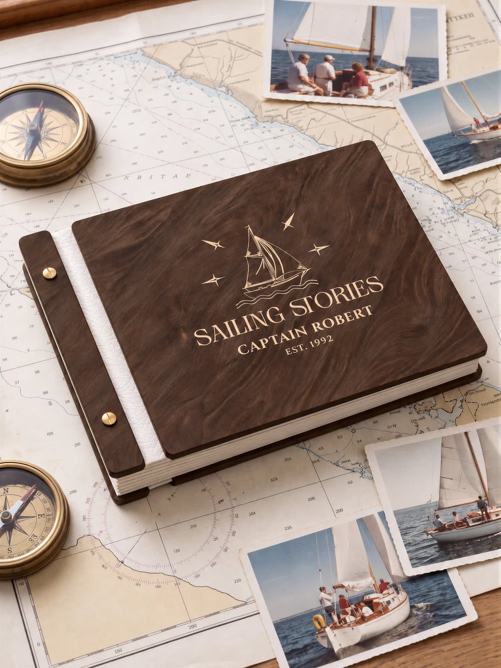 Jacobean wooden album with cream laser engraving of sailboat, waves and compass stars. The full personalized cover rests on a styled surface, with ivory binding and gold screws.