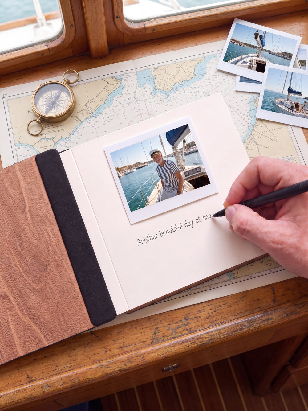 An open Hazelnut album with a photograph on a cream page. A hand writes a memory beneath it; a flat black fabric strip runs along the inner wooden cover.
