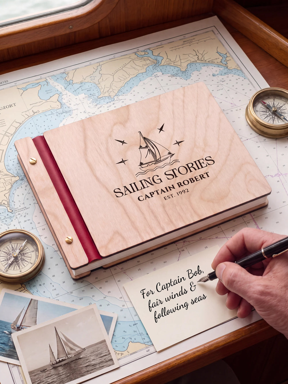 A Natural wooden album with the SAILING STORIES engraving, cherry red binding and gold screws. A hand writes on a separate gift card beside the book.